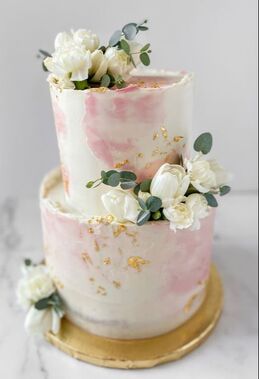 Picture of a 6 inch round cake on an 8 inch cake. Decorated with smooth buttercream but rough edges. Pink watercolor buttercream smears, white tulips, eucalyptus greenery , and gold leaf complete the look.