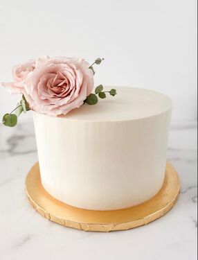Picture of an 8 inch round cake with smooth and sharp white buttercream. With 3 dainty blush colored roses and greenery placed on the top left.