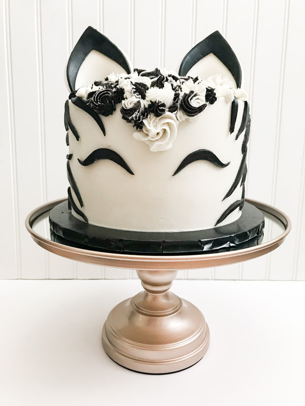 Picture of an 8 inch cake, decorated to resemble a zebra. fondant stripes, eyes, and ears, with a black and white buttercream mane.