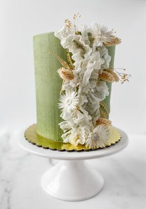 Picture - A tall 6 inch round cake with sage green buttercream with fried rice paper sails and fried florals going up the side. On a ceramic white 9